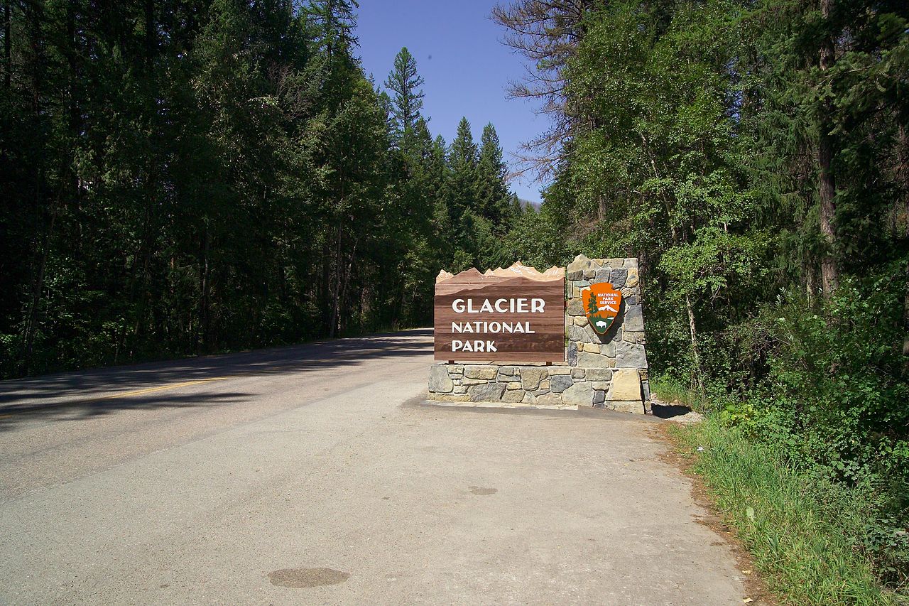 Glacier National Park entrance sign in the woods on dirt road.