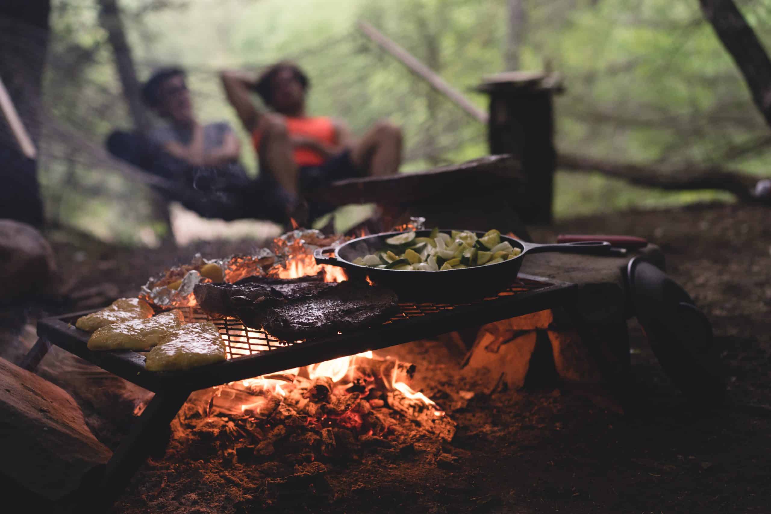 Open pan on fire full of vegetables while campers in back.