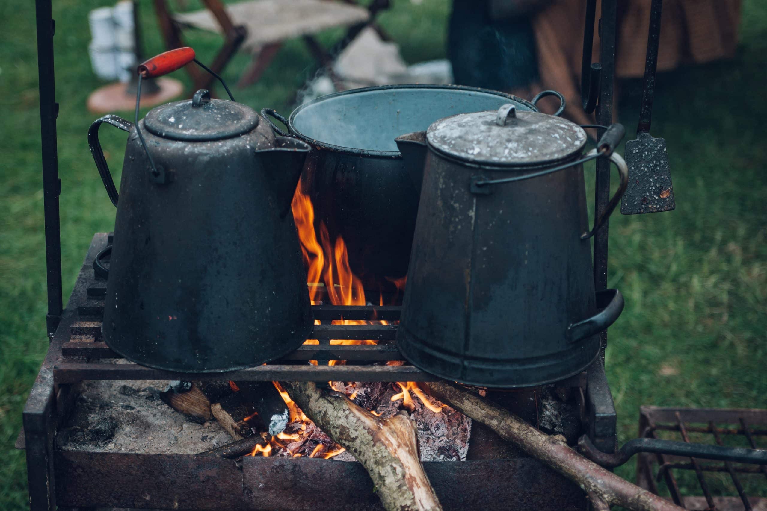 Three vessels heating water over an outdoor fire.